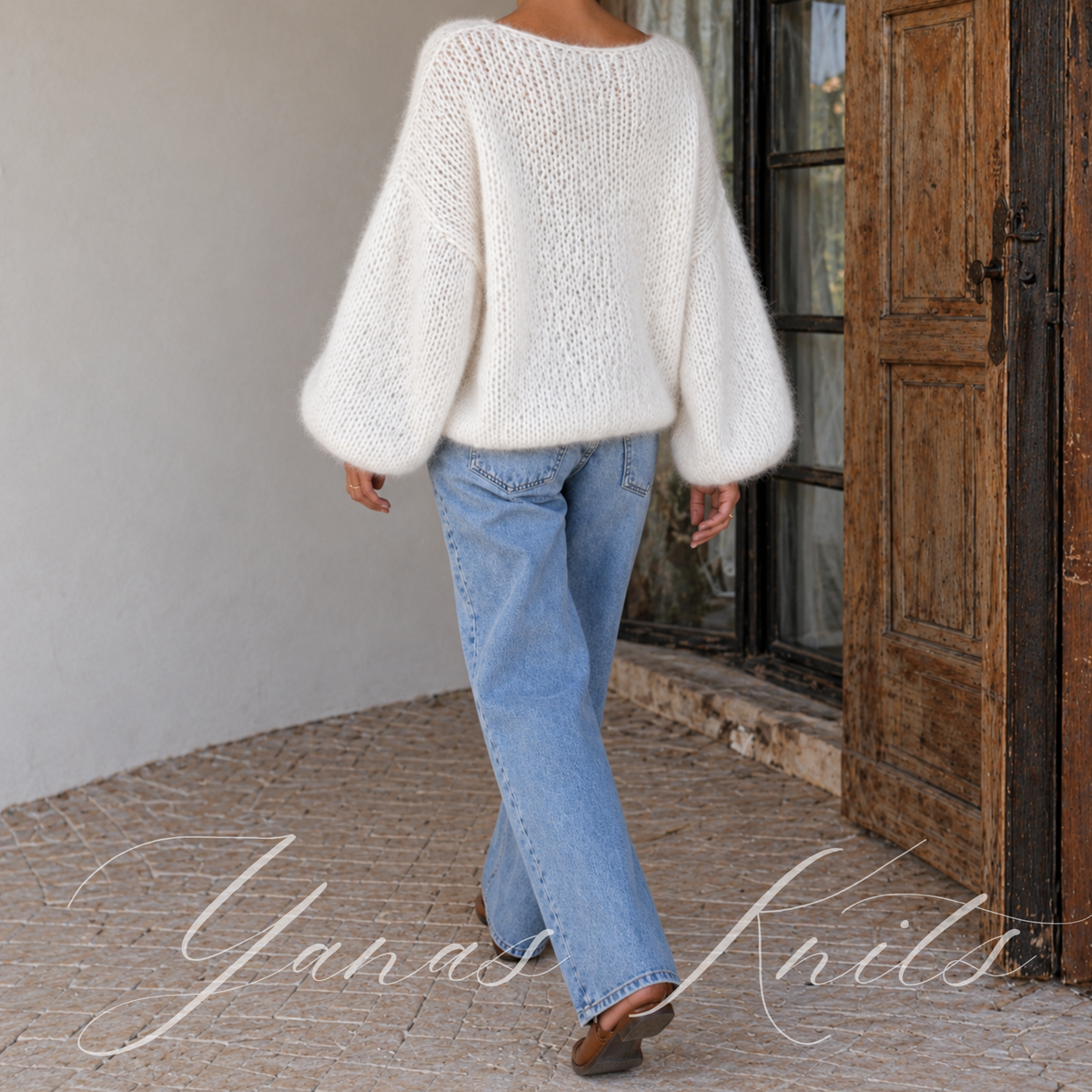 Full back view of an ivory loose knit pullover with balloon sleeves worn with jeans