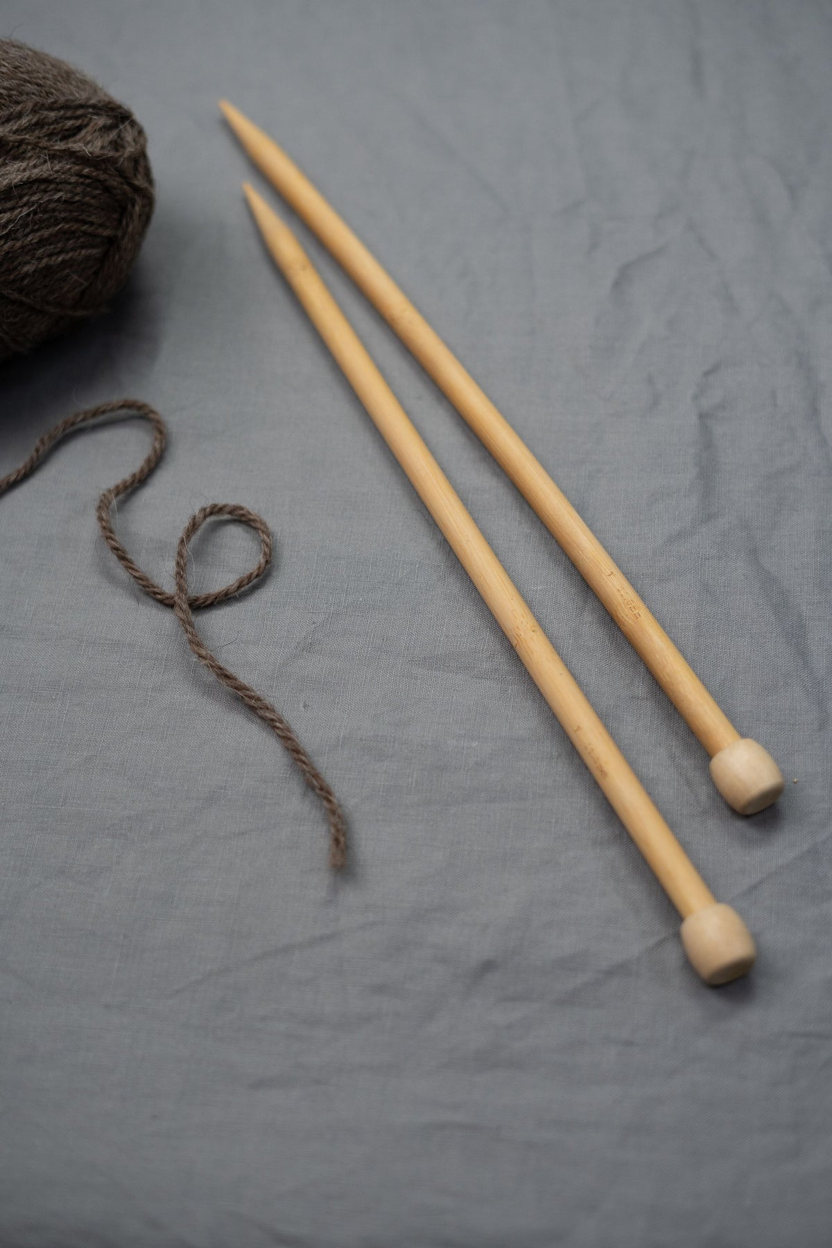 A pair of wooden knitting needles and brown yarn on soft grey linen