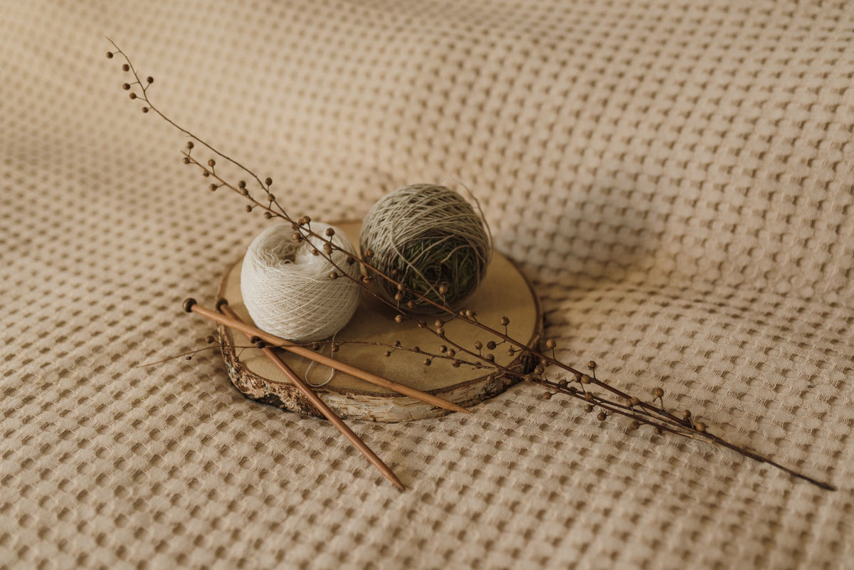 Ivory and oatmeal yarn with wooden knitting needles on natural textured linen